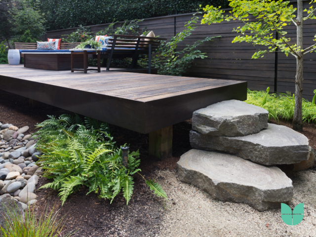 A contemporary style garden with stone chairs, plants, and a decking with a bench and table